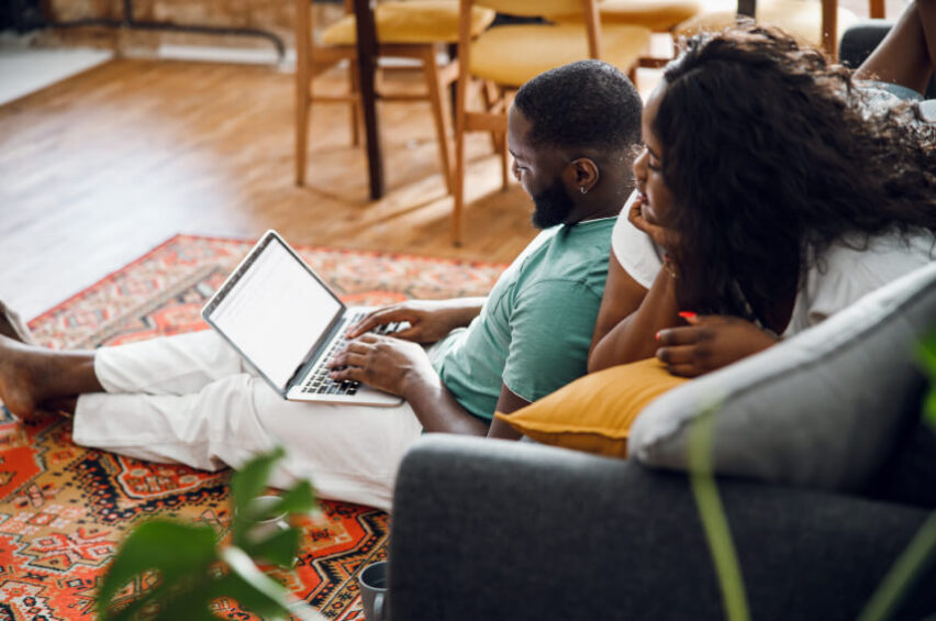 man woman seated on floor and sofa at home in living room looking at laptop